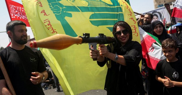 A woman holds a mock-up of a rocket-propelled grenade (RPG) next to a Hezbollah flag during the Arbaeen rally in Tehran, Iran, Aug. 4, 2026. (Reuters Photo)