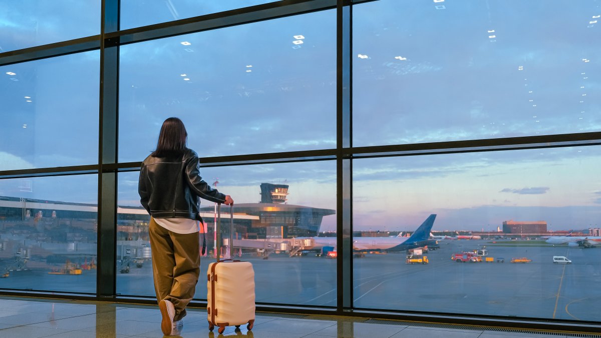 A young woman waits with her suitcase by an airport window as she prepares to board a flight. (Shutterstock Photo)