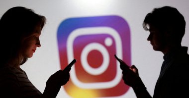 Teenagers pose for a photo while holding smartphones in front of an Instagram logo in this illustration created Sept. 11, 2025. (Reuters Photo)