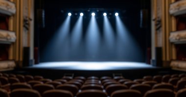 Empty theater stage with spotlights illuminating the center, rows of unoccupied seats visible in the foreground. (Shutterstock Photo)
