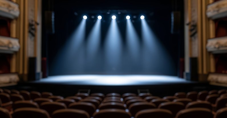 Empty theater stage with spotlights illuminating the center, rows of unoccupied seats visible in the foreground. (Shutterstock Photo)