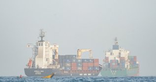 People sail their boat past container ships anchoring near the Strait of Bab al-Mandeb off Yemen's coast in the Gulf of Aden, Aug. 6, 2026. (AFP Photo) 