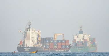 People sail their boat past container ships anchoring near the Strait of Bab al-Mandeb off Yemen's coast in the Gulf of Aden, Aug. 6, 2026. (AFP Photo) 