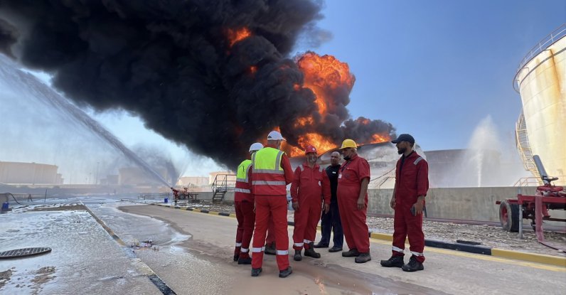 Workers stand near the scene as flames and thick smoke rise from a burning fuel storage tank at the Zawiya oil depot, west of Tripoli, Libya, Aug. 11, 2026. (EPA Photo)