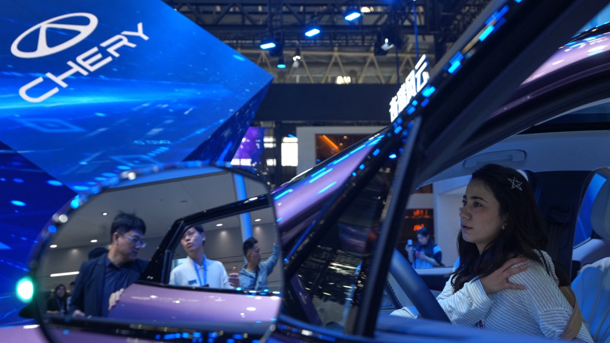 A woman tries out the Chinese automaker Chery T9L model as a staff member attends to a visitor at the Chery exhibition booth during the Auto China 2026, Beijing, China, April 25, 2026. (AP Photo)