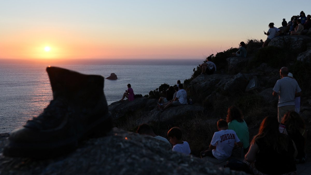Pilgrim Boot sculpture is pictured near tourists looking at the sunset the day before the solar eclipse, on the Costa da Morte ("Coast of Death"), once considered the end of the world and a traditional destination for pilgrims completing the Camino de Santiago, in northwestern Spain, Aug. 11, 2026. (Reuters Photo)