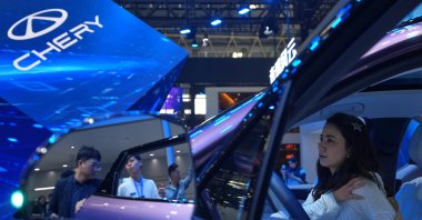 A woman tries out the Chinese automaker Chery T9L model as a staff member attends to a visitor at the Chery exhibition booth during the Auto China 2026, Beijing, China, April 25, 2026. (AP Photo)