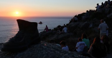 Pilgrim Boot sculpture is pictured near tourists looking at the sunset the day before the solar eclipse, on the Costa da Morte ("Coast of Death"), once considered the end of the world and a traditional destination for pilgrims completing the Camino de Santiago, in northwestern Spain, Aug. 11, 2026. (Reuters Photo)