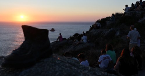 Pilgrim Boot sculpture is pictured near tourists looking at the sunset the day before the solar eclipse, on the Costa da Morte ("Coast of Death"), once considered the end of the world and a traditional destination for pilgrims completing the Camino de Santiago, in northwestern Spain, Aug. 11, 2026. (Reuters Photo)