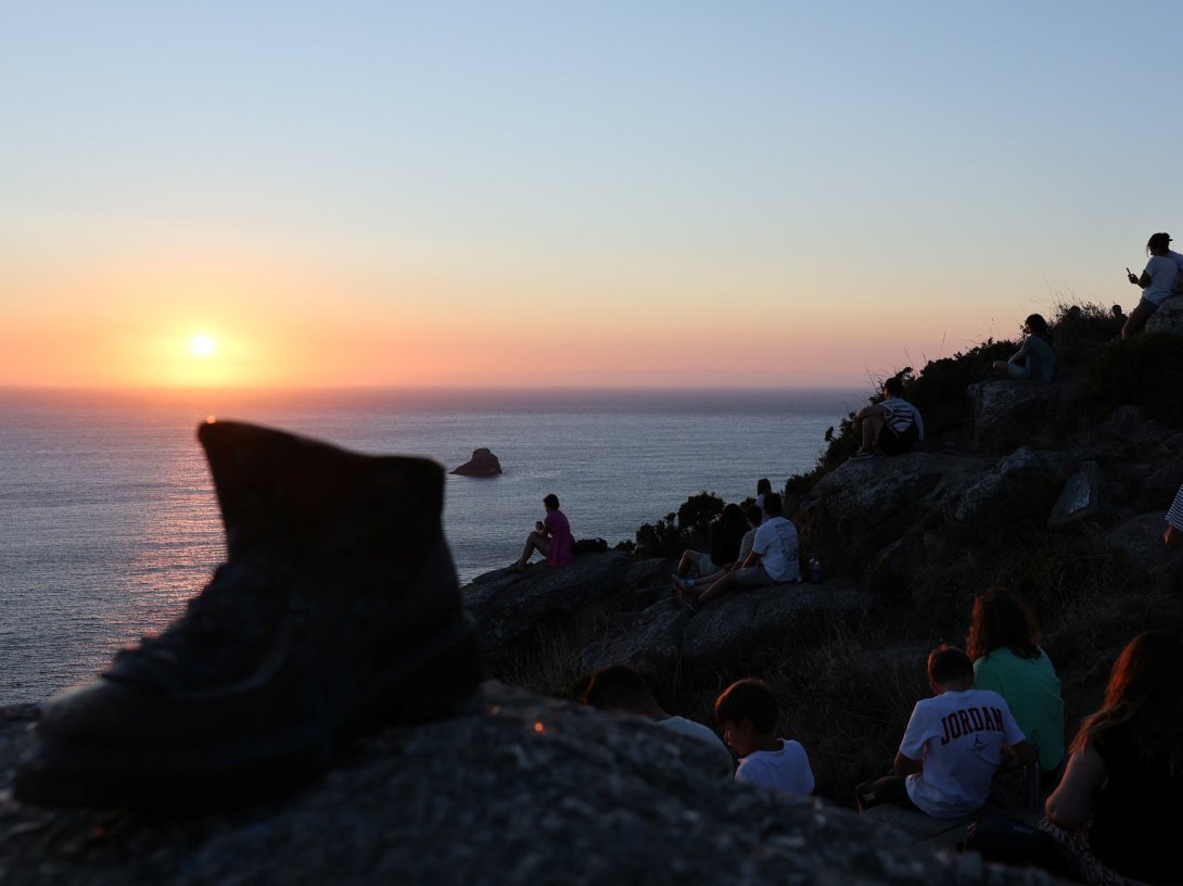 Pilgrim Boot sculpture is pictured near tourists looking at the sunset the day before the solar eclipse, on the Costa da Morte ("Coast of Death"), once considered the end of the world and a traditional destination for pilgrims completing the Camino de Santiago, in northwestern Spain, Aug. 11, 2026. (Reuters Photo)