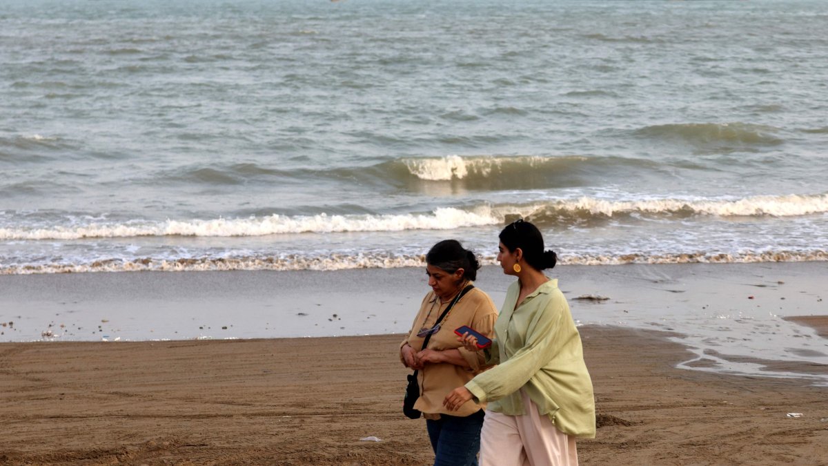 Two women walk along the seashore, as vessels are seen in the Strait of Hormuz off the port city of Bandar Abbas, in southern Iran, Aug. 10, 2026. (AFP Photo)