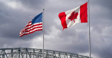 The U.S. and Canada flags flutter next to the Blue Water Bridge border crossing in Point Edward, Ontario, Oct. 24, 2025. (AFP Photo)