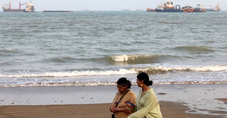 Two women walk along the seashore, as vessels are seen in the Strait of Hormuz off the port city of Bandar Abbas, in southern Iran, Aug. 10, 2026. (AFP Photo)