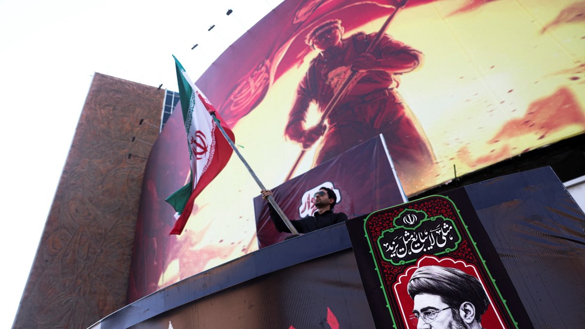 A man holds an Iranian flag, next to a picture of Iran's Supreme Leader Mojtaba Khamenei in Tehran, Iran, Aug. 13, 2026. (Reuters Photo)