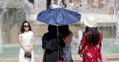 People shelter from the sun under an umbrella on a hot summer day, Milan, Italy, July 31, 2026. (EPA Photo)