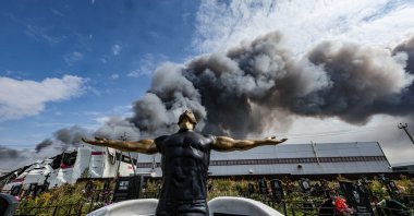 A statue is seen as smoke rises above a Wildberries facility behind, following a Ukrainian drone strike near Podolsk, Moscow Region, Russia, Aug. 16, 2026. (EPA Photo)