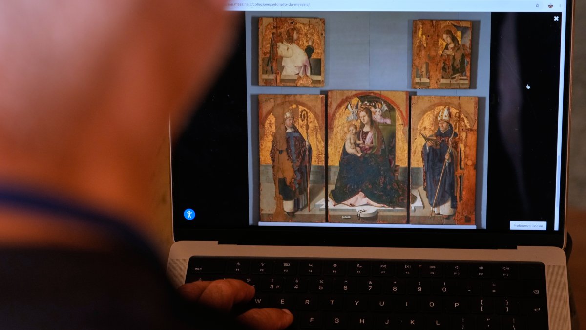 A journalist browses the Messina museum website showing a picture of the Early Renaissance painter Antonello da Messina's artwork, where three of the five panels belonging to the Polyptych of San Gregorio and the double-sided panel with the Madonna and the Christ in Pietà, stolen from the Sicilian museum on Aug. 15, Rome, Italy, Aug. 16, 2026. (AP Photo)