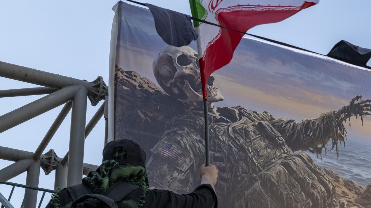 A person carries an Iranian national flag in front of an anti-U.S. billboard hanging from a bridge in southern Tehran, Iran, Aug. 4, 2026. (Getty Images Photo)