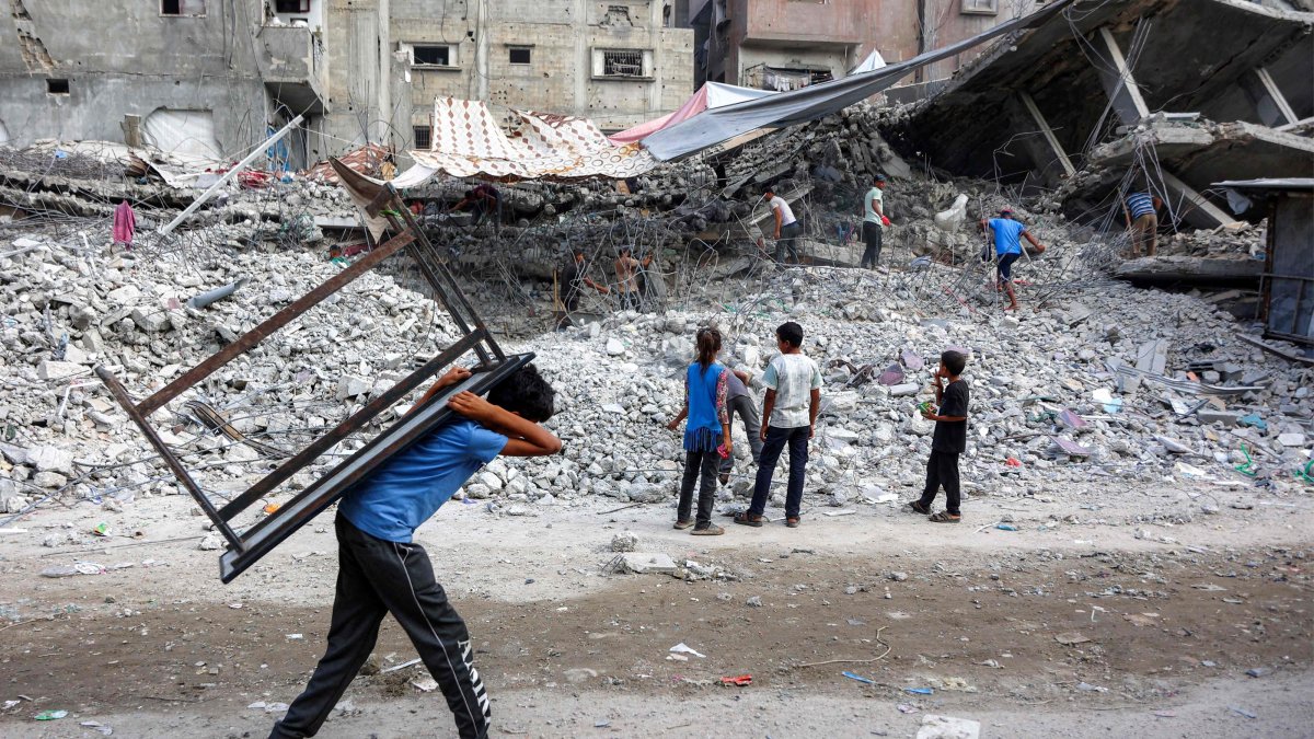 A boy walks carrying a table on his back past salvage workers scrapping the rubble of a building that was destroyed during Israel's attacks, Gaza City, Palestine, Aug. 16, 2026. (AFP Photo)