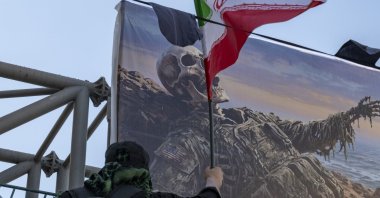 A person carries an Iranian national flag in front of an anti-U.S. billboard hanging from a bridge in southern Tehran, Iran, Aug. 4, 2026. (Getty Images Photo)