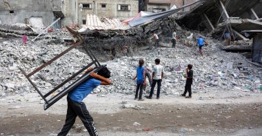 A boy walks carrying a table on his back past salvage workers scrapping the rubble of a building that was destroyed during Israel's attacks, Gaza City, Palestine, Aug. 16, 2026. (AFP Photo)