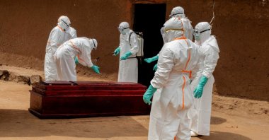 Community-based health workers in personal protective equipment (PPE) disinfect a wooden coffin carrying the body of a man who died of Ebola in Bunia, Congo, July 10, 2026. (Reuters Photo)