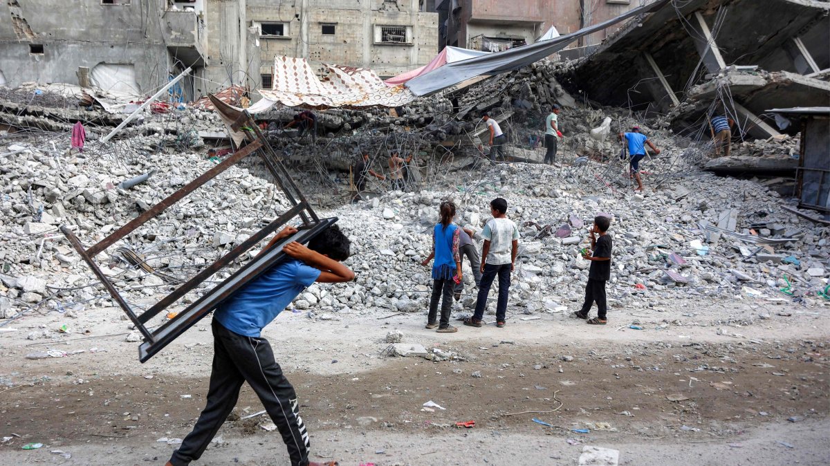 A boy walks carrying a table on his back past salvage workers scrapping the rubble of a building destroyed in Israel's war in Gaza, Palestine. (AFP Photo)