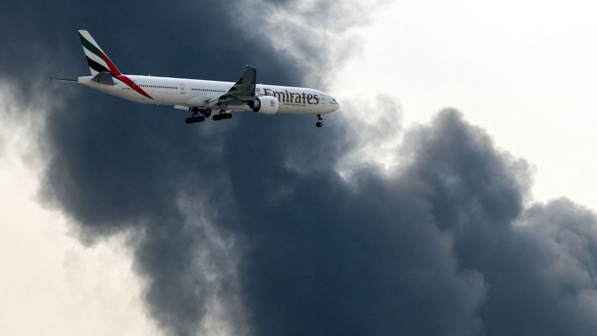 An Emirates Airbus A350 aircraft prepares for landing as a smoke plume rises from an ongoing fire at Dubai International Airport in Dubai, UAE, March 16, 2026. (AFP File Photo)