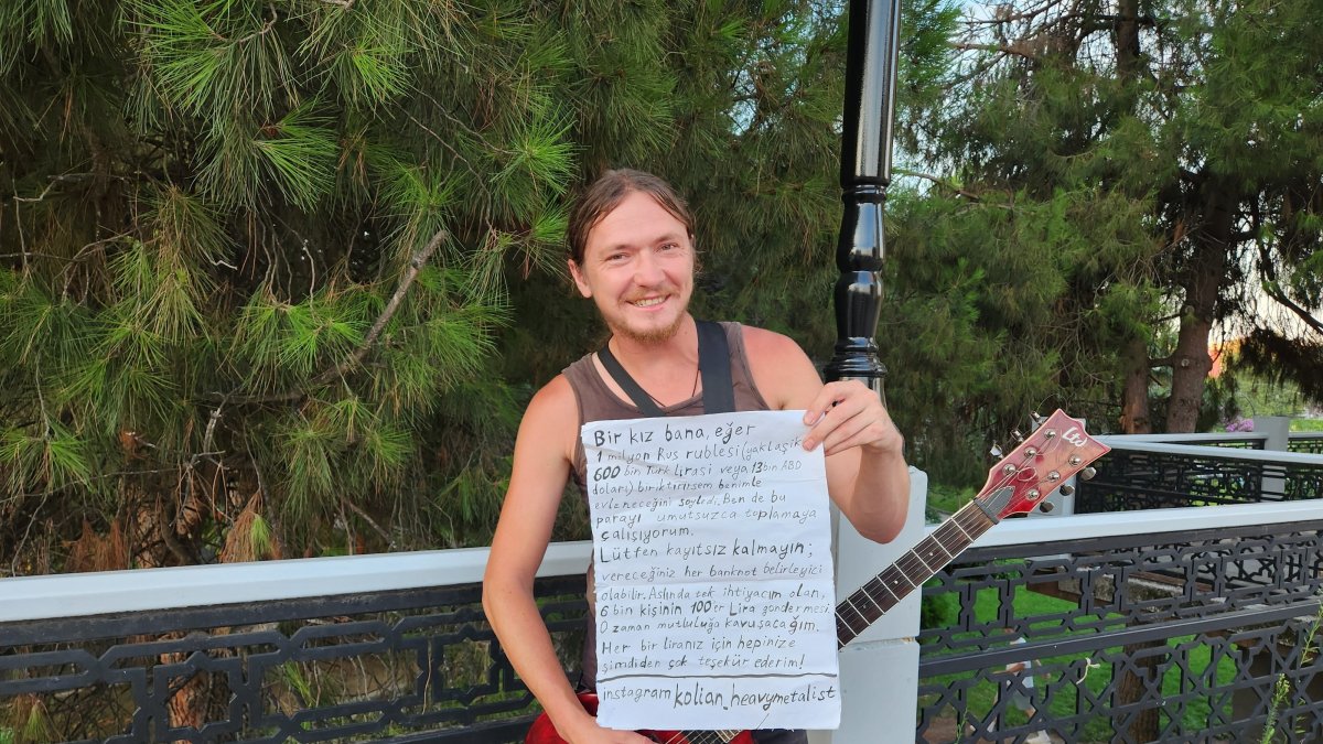 Nikolay Gromkov plays guitar while displaying his handwritten Turkish note, Samsun, Türkiye, Aug. 19, 2026. (IHA Photo)