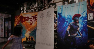 A child looks at a drawing poster promoting a Chinese animated film "Niu Lai" on display with other movie posters at a cinema, Beijing, China, Aug. 18, 2026. (AP Photo)