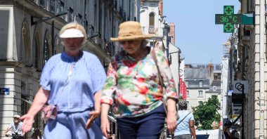 People walk down a street as a pharmacy thermometer indicates a temperature of 36 Celsius degrees as a heat wave hits France, downtown Nantes, France, June 19, 2025. (AFP Photo)