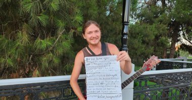 Nikolay Gromkov plays guitar while displaying his handwritten Turkish note, Samsun, Türkiye, Aug. 19, 2026. (IHA Photo)