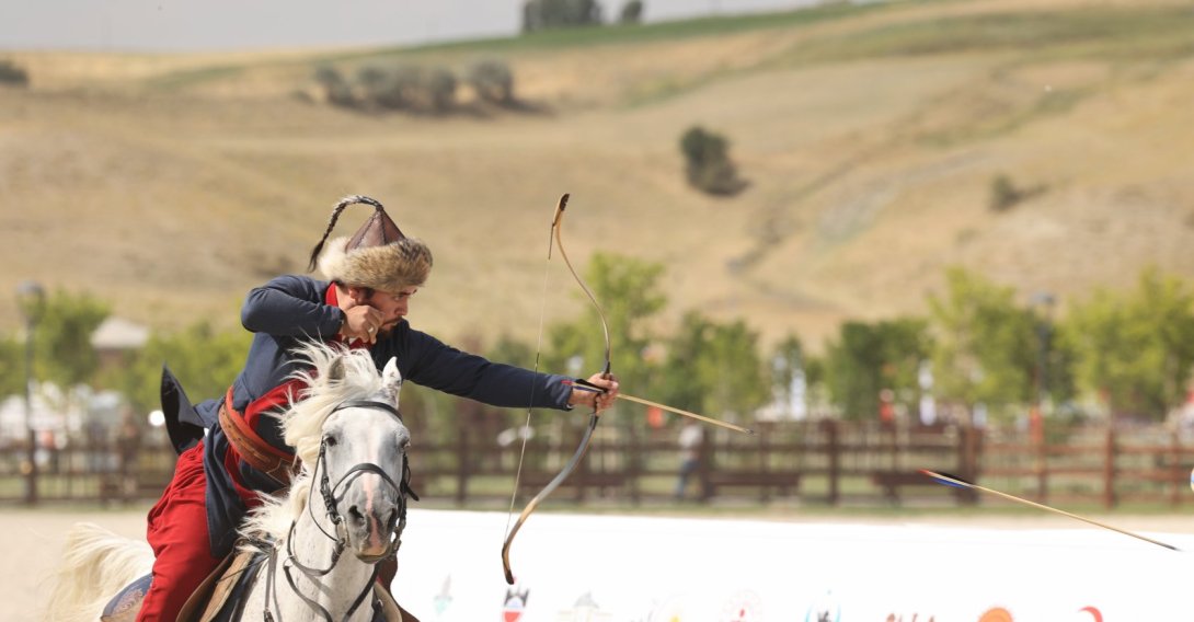 A competitor dressed in traditional clothing performs mounted archery on a galloping white horse. (Courtesy of Okçular Vakfı)