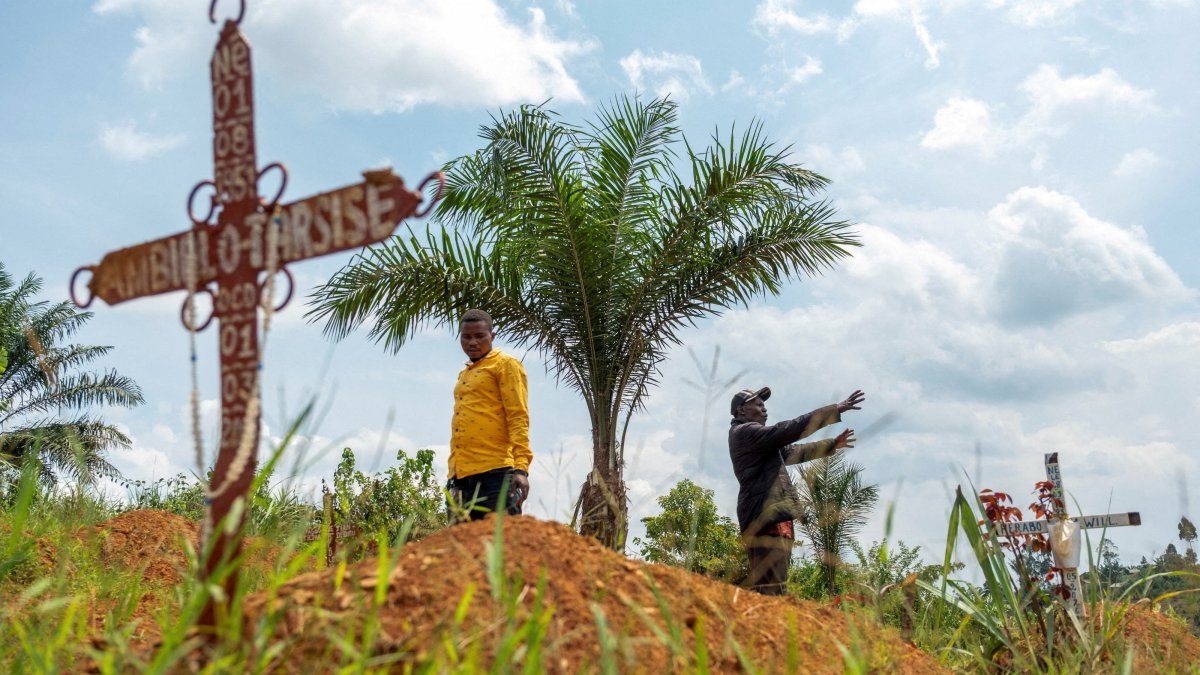 Charles Mambo, the supervisor at the Ceca-20 cemetery, flanked by the assistant warden of the cemetery, stands, Mungwalu, Ituri province, Democratic Republic of Congo, July 14, 2026. (Reuters Photo)