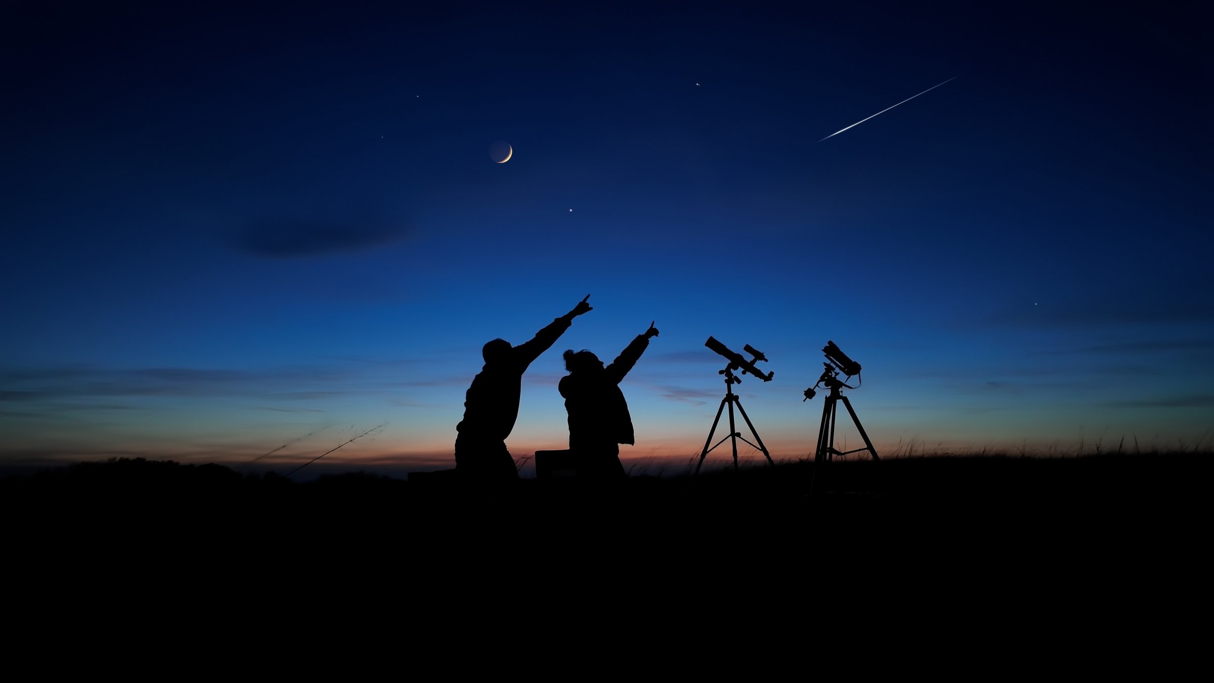 Amateur astronomers looking at the evening sky, observing planets, stars and the moon with a telescope. (Shutterstock Photo)