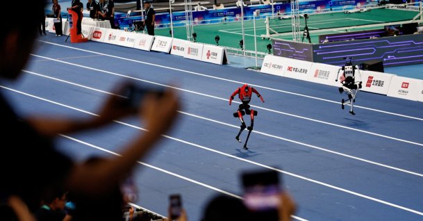 Spectators use smartphones as they watch humanoid robots by Honor and Tiangong compete during a 100-meter large-sized group preliminary race, at the 2026 World Humanoid Robot Games, in Beijing, China, Aug. 22, 2026. (Reuters Photo)