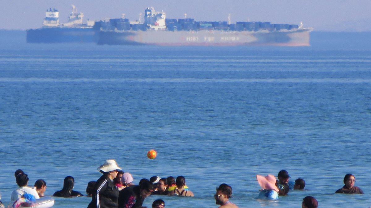 Holidaymakers swim as ships cross the Gulf of Suez toward the Red Sea at al Sokhna beach in Suez, Egypt, Aug. 10, 2026. (AP Photo)