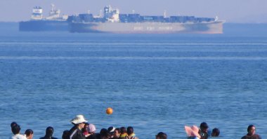 Holidaymakers swim as ships cross the Gulf of Suez toward the Red Sea at al Sokhna beach in Suez, Egypt, Aug. 10, 2026. (AP Photo)