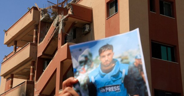 A damaged building in the background while a person holds a picture of Moaz Abu Taha, as Palestinian journalists take part in a solidarity vigil to commemorate their colleagues killed during an Israeli strike at Nasser Hospital, on the first anniversary of their killing, in Khan Younis, southern Gaza Strip, Palestine, Aug. 25, 2026. (Reuters Photo)