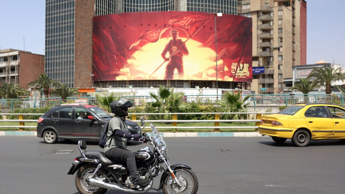An Iranian rides a motorbike past a political billboard displayed at the Valiasr square in Tehran, Iran, Aug. 17, 2026.  (EPA Photo)