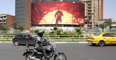 An Iranian rides a motorbike past a political billboard displayed at the Valiasr square in Tehran, Iran, Aug. 17, 2026.  (EPA Photo)