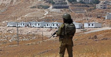 An Israeli soldier stands guard against the backdrop of an illegal Israeli settlement outpost in Beit Sahur, south of Bethlehem, in the occupied West Bank, Aug.14, 2026. (AFP Photo)