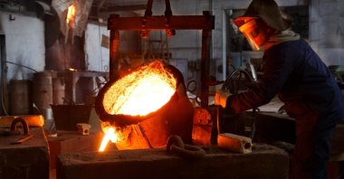 Industrial worker in protective gear pours molten metal at a steel foundry. (Shutterstock Photo)