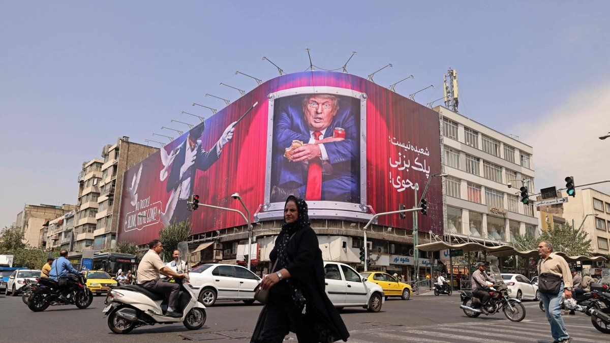 A pedestrian walks past a billboard depicting U.S. President Donald Trump inside a catering container, installed on a building along a street in downtown, Tehran, Iran, Aug. 31, 2026. (AFP Photo)