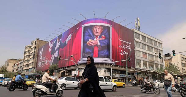 A pedestrian walks past a billboard depicting U.S. President Donald Trump inside a catering container, installed on a building along a street in downtown, Tehran, Iran, Aug. 31, 2026. (AFP Photo)