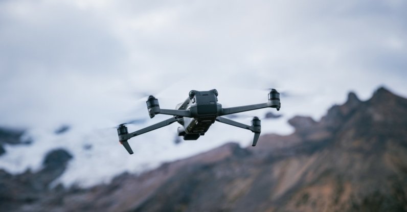 A drone flies with mountain tops in the background. (Shutterstock Photo)