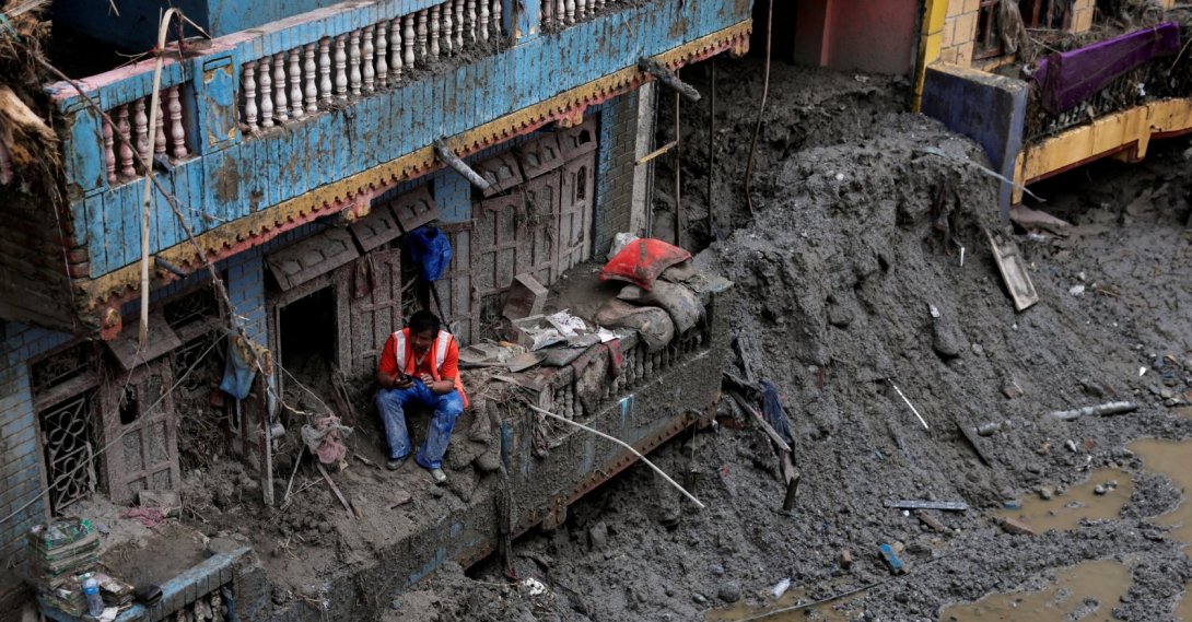 A man uses his mobile phone as he sits outside a damaged house following the deadly flash floods and mudslides in Devighat, Nuwakot district, Nepal, Sept. 5, 2026. (Reuters Photo)