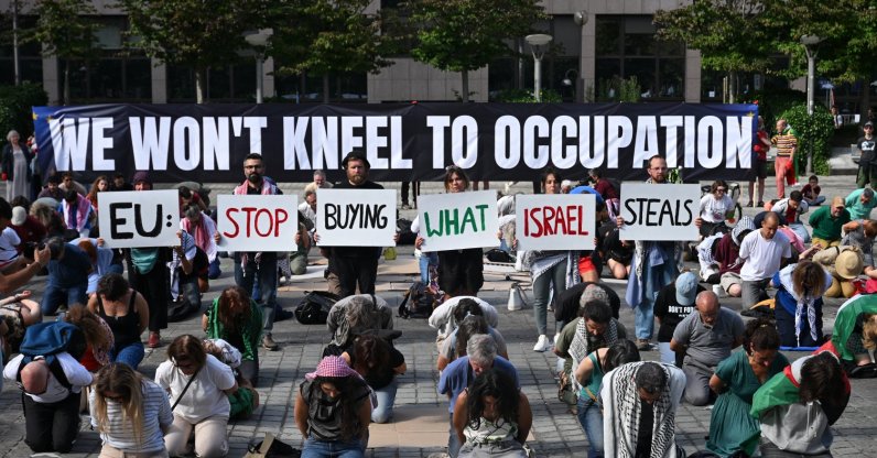 Flotilla for Gaza activists hold placards reading "EU: stop buying what Isreal steals" among protesters and in front of a banner that reads: “We won't kneel to occupation”, during a demonstration to demand EU leaders to ban goods from illegal Israeli settlements, in Brussels on June 17, 2026. (AFP File Photo)