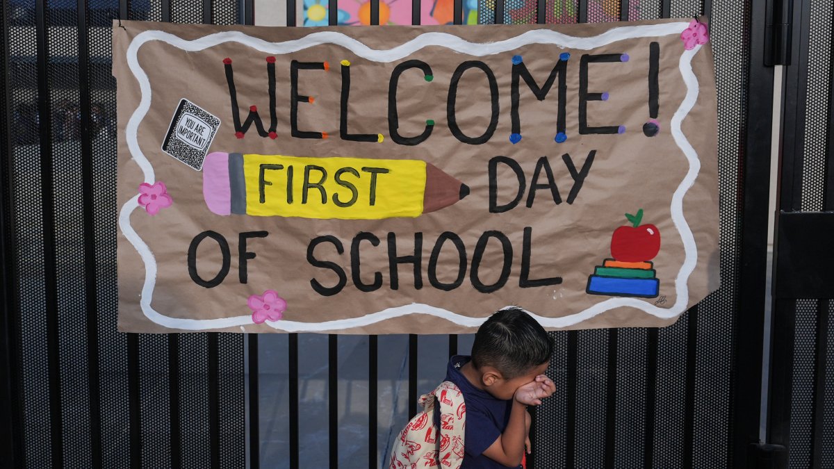 A student wipes his face while his mother takes a photo of him with a sign on the first day of school at Betsy Ross Elementary School, California, U.S., Aug. 6, 2026. (AP Photo)