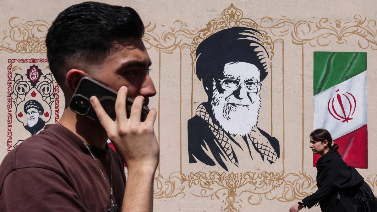 People walk past a wall decorated with the image of the assassinated Iranian supreme leader Ayatollah Ali Khamenei and the national flag, Tehran, Iran, Sept. 14, 2026. (AFP Photo)